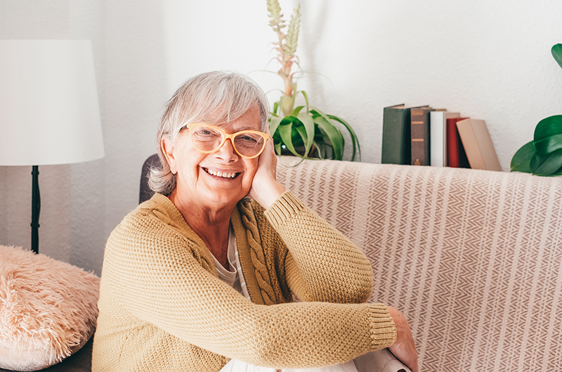 Carefree Gray Haired Senior Woman in Eyeglasses Sitting Relaxed on Home Sofa Looking at Camera Smiling